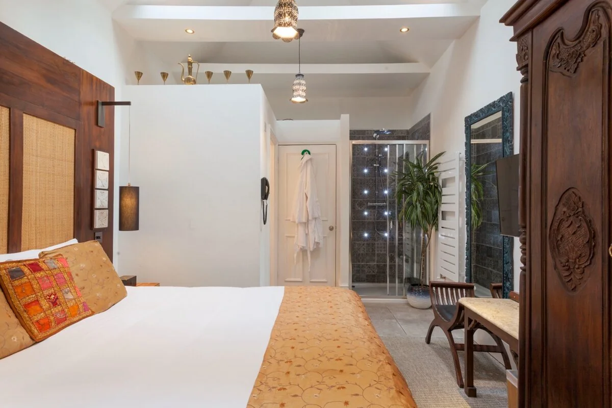 Zanzibar House bedroom with carved wood headboard, Moroccan lanterns and open ensuite shower