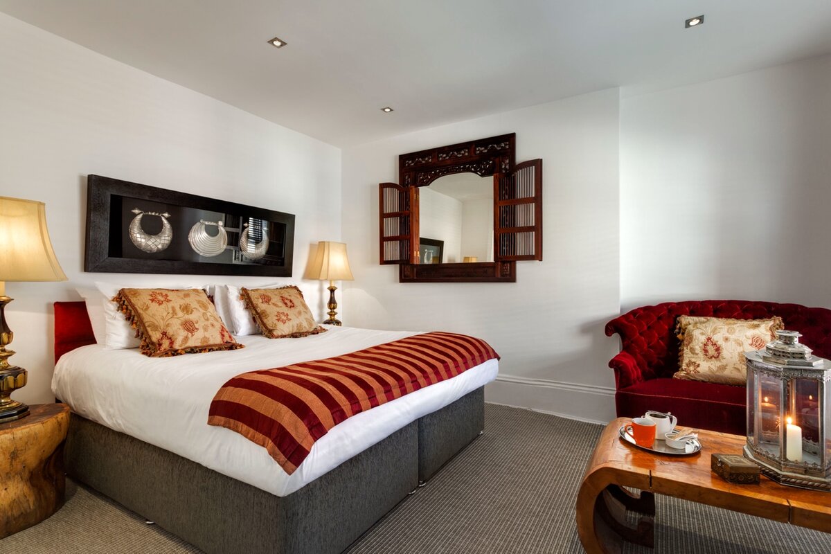 India — king bed with red velvet chesterfield, carved mirror and warm lighting